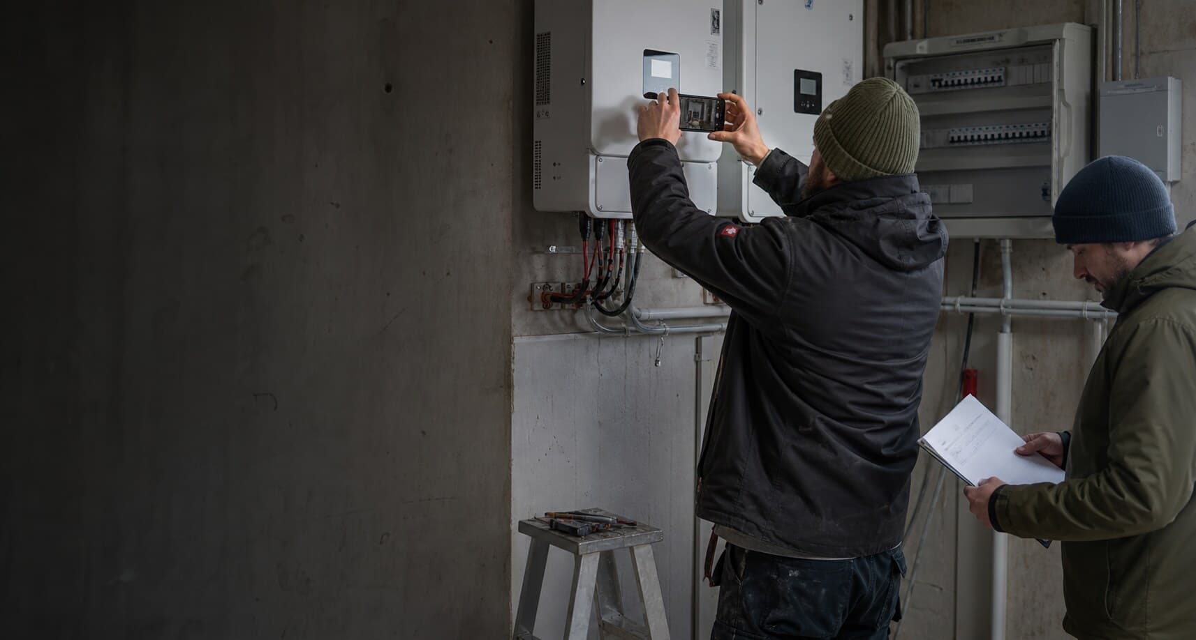 Technician photographing completed solar equipment while a reviewer checks the installation record