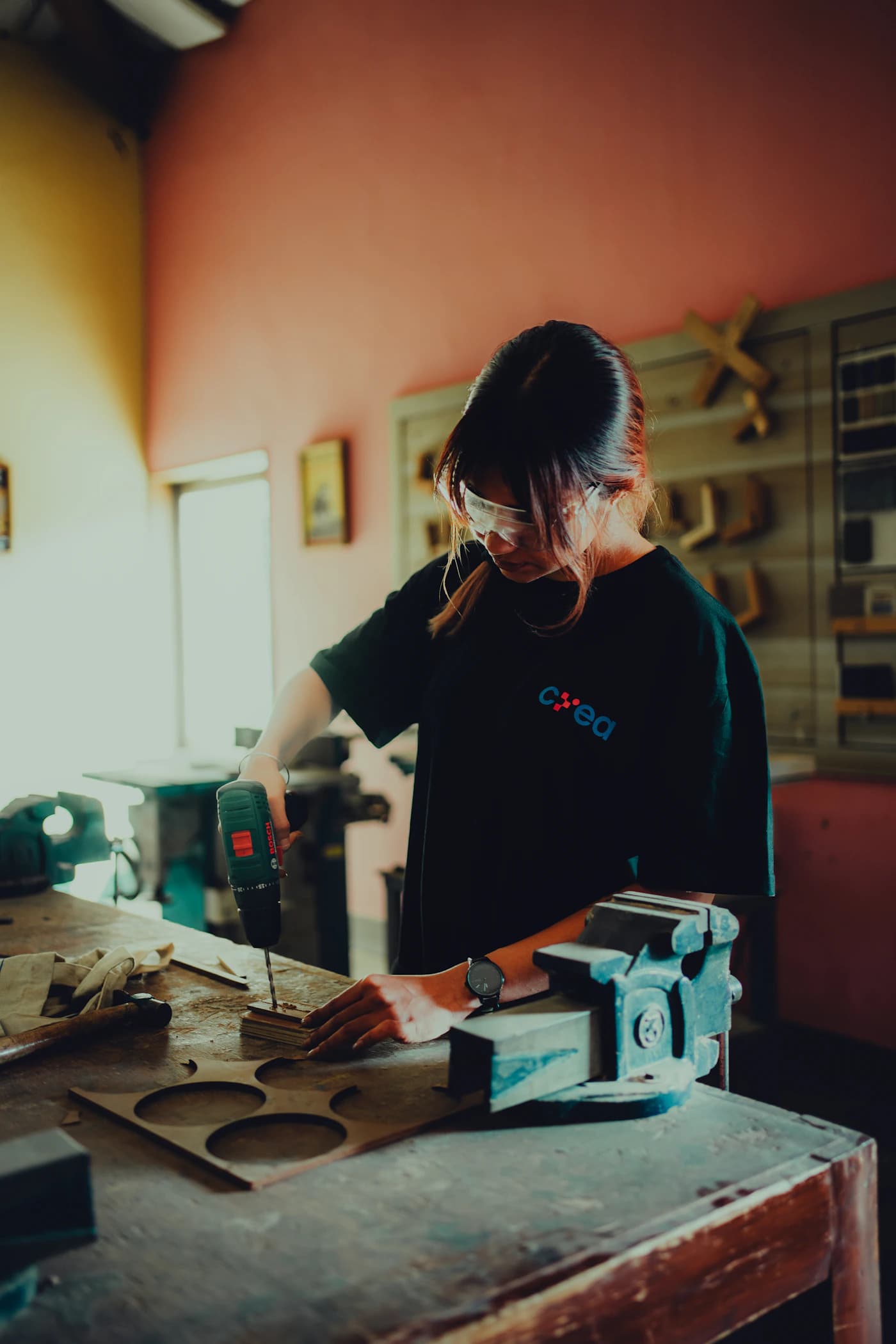 A maker drilling a wooden piece at a workbench